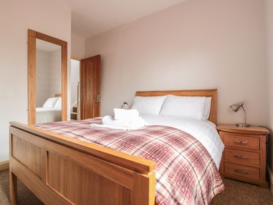 A bedroom with a wooden bed, a bedside table with a lamp, a full-length mirror, and an open wooden door at 33 Crescent Gardens in Bath