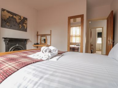 A bedroom with a bed with striped white linens a folded plaid blanket and rolled white towels a world map on the wall a fireplace a wooden shelf with a mirror and a full-length mirror near an open door at 33 Crescent Gardens in Bath