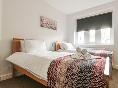 A bedroom with two single beds with blankets and rolled towels in front of a window with a black blind at 33 Crescent Gardens in Bath