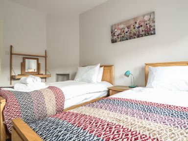 A bedroom with two single beds a bedside table with a lamp a wall-mounted mirror and a floral painting at 33 Crescent Gardens in Bath