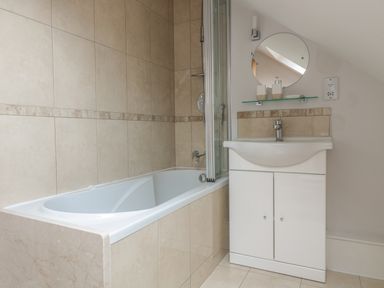 A bathroom with a bathtub, a white vanity with a basin and faucet, a round mirror, and tiled walls at 33 Crescent Gardens Bath