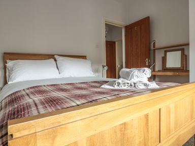 A bedroom with a wooden bed with white pillows and a plaid blanket with rolled towels on top at 33 Crescent Gardens in Bath