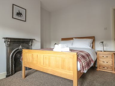 A bedroom with a wooden bed frame, white bedding, folded towels, a wooden nightstand with a lamp, and a decorative black fireplace at 33 Crescent Gardens in Bath