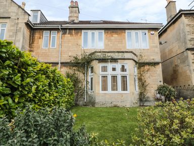 Front view of a two-story stone house with multiple windows and a small garden with green shrubs and grass at 33 Crescent Gardens in Bath