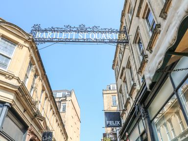 A street view with a metal sign reading Bartlett St Quarter above the road between two stone buildings at 33 Crescent Gardens in Bath