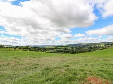 A green field with trees and hills under a cloudy sky at Mountain View in Rhayader