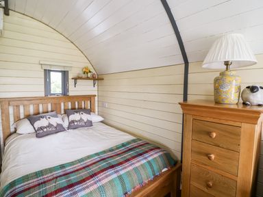 A bedroom with a wooden bed and dresser a lamp and decorative items on the dresser a small window and a shelf with flowers at Mountain View in Rhayader