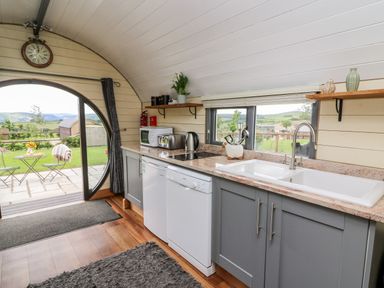 A kitchen with grey cabinets a white sink dishwasher microwave and toaster with a door leading to a patio at Mountain View in Rhayader