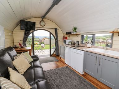 A small living area with a leather sofa and kitchen with appliances and a round door opening to a garden at Mountain View in Rhayader