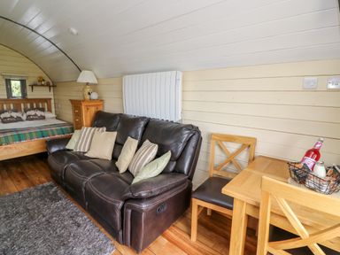 A living area with a brown leather sofa and cushions a wooden dining table with chairs a bed with pillows and a blanket and a wooden dresser with a lamp at Mountain View in Rhayader