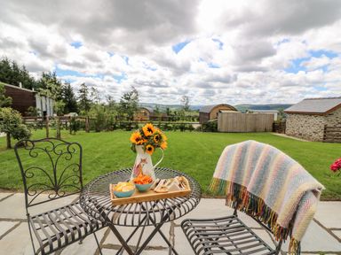 A patio with a metal table and chairs with food and flowers on the table and a blanket on one chair at Mountain View in Rhayader