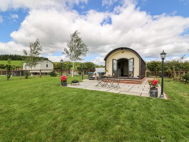 A small cabin with an open door on a stone patio with table and chairs and flowers on grass at Mountain View in Rhayader