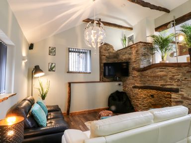 A living room with black and white sofas a wall mounted tv and exposed stone walls at Elvan Cottage in Liskeard