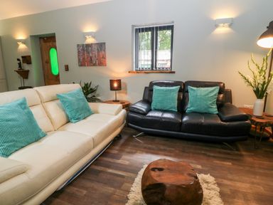A living room with two sofas with turquoise cushions a wooden coffee table and a window at Elvan Cottage in Liskeard