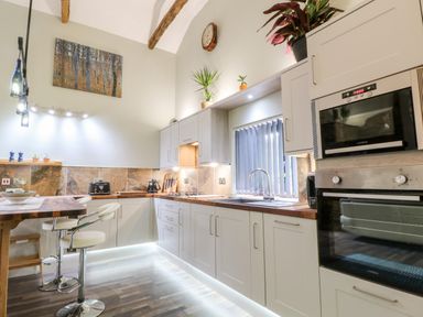 A kitchen with white cabinets wooden countertops a built in oven microwave and two bar stools at Elvan Cottage in Liskeard