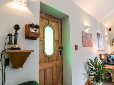 A wooden door with a frosted glass panel next to a wall-mounted vintage telephone and an old-fashioned candlestick phone in a living room with a plant and a painting at Elvan Cottage in Liskeard