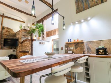 A kitchen with a wooden countertop and white stools near a stone wall and ceiling beams at Elvan Cottage in Liskeard