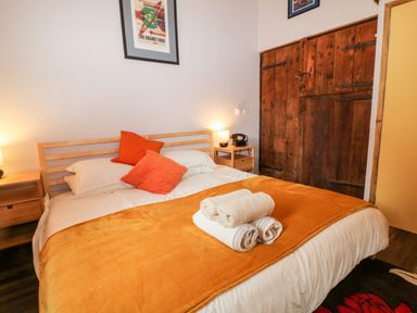 A bedroom with a double bed with orange bedding and pillows two wooden nightstands lamps and a wooden closet door at Elvan Cottage in Liskeard