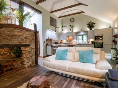 An open living room and kitchen area with a white sofa and blue cushions a wooden coffee table exposed wooden beams and stone wall at Elvan Cottage in Liskeard