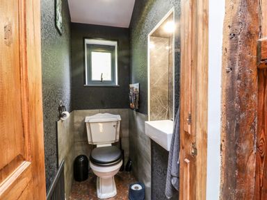 A small bathroom with a toilet a sink a window and wooden door at Elvan Cottage in Liskeard