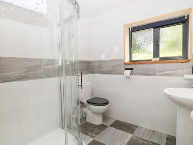 A bathroom with a glass shower enclosure a toilet with a black seat a sink and a window with frosted glass at Elvan Cottage in Liskeard