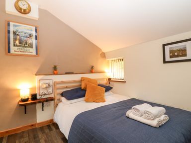 A bedroom with a bed with pillows and towels on it and framed pictures on the walls at Elvan Cottage in Liskeard