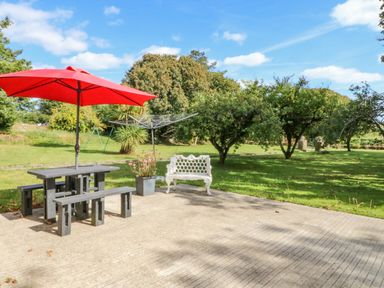 A patio with a picnic table and red umbrella a white bench and a rotary clothesline in a garden at Beehive Cottage Kilbrittain County Cork