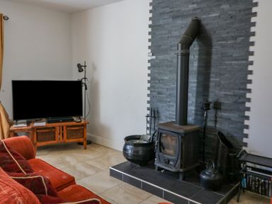 A living room with a red sofa a television on a wooden stand and a wood-burning stove on a tiled hearth at Beehive Cottage in Kilbrittain County Cork