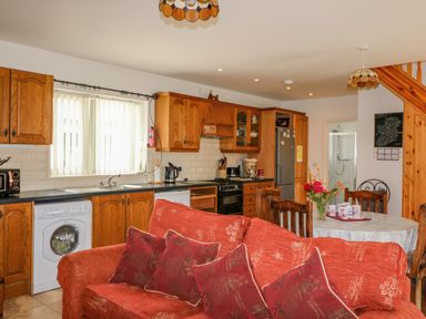 A kitchen and dining area with wooden cabinets red sofa and round dining table at Beehive Cottage in Kilbrittain County Cork