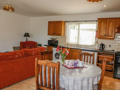 A kitchen and dining area with wooden cabinets a round table with cups and flowers and a red couch at Beehive Cottage in Kilbrittain County Cork