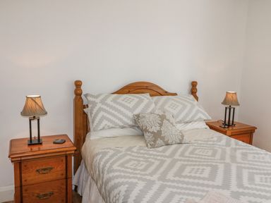 A bedroom with a double bed patterned bedding wooden headboard and two wooden bedside tables with lamps at Beehive Cottage in Kilbrittain County Cork