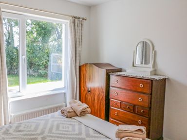 A bedroom with a bed with folded towels near a window and a wooden dresser with a mirror at Beehive Cottage in Kilbrittain County Cork