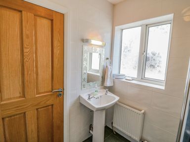 A bathroom with a wooden door a pedestal sink a mirror a towel ring a radiator and a window with floral frosted glass at Beehive Cottage Kilbrittain County Cork