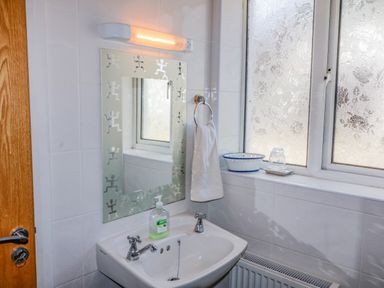 A bathroom sink with soap dispenser hand towel and decorated mirror next to frosted windows at Beehive Cottage in Kilbrittain County Cork