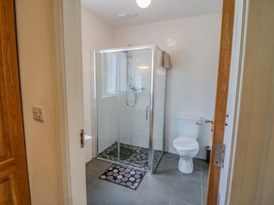 A bathroom with a glass shower enclosure a toilet and a bath mat on the floor at Beehive Cottage Kilbrittain County Cork