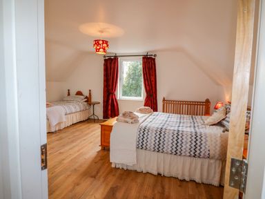 A bedroom with two beds a wooden crib a window with red curtains and wooden flooring at Beehive Cottage in Kilbrittain County Cork