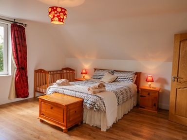 A bedroom with a double bed a wooden chest bedside tables a baby crib and red curtains at Beehive Cottage in Kilbrittain County Cork