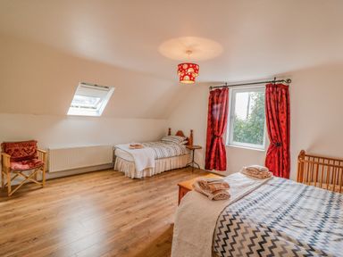 A bedroom with two beds a wooden chair a window with red curtains and wooden flooring at Beehive Cottage in Kilbrittain County Cork