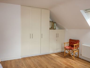 A room with white wardrobes wooden floor a wooden chair with red cushions and a window on the ceiling at Beehive Cottage in Kilbrittain County Cork