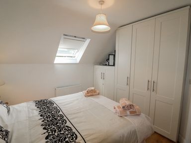A bedroom with a bed with black and white bedding towels on the bed and white wardrobes under a sloped ceiling with a skylight window at Beehive Cottage in Kilbrittain County Cork