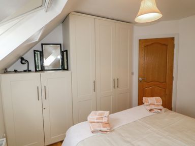 A bedroom with white wardrobes a wooden door a bed with folded towels and a mirror on a cabinet at Beehive Cottage in Kilbrittain County Cork