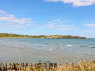 A coastal view with calm sea waves grass and wooden posts at Beehive Cottage in Kilbrittain County Cork