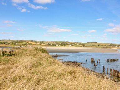 A coastal landscape with grassy dunes wooden benches and a sandy beach with water at Beehive Cottage in Kilbrittain County Cork