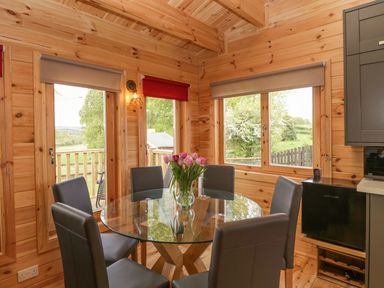A dining area with a round glass table surrounded by six chairs and a vase with flowers at Sunnyside Lodge in Crewkerne