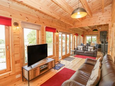 A wooden living room with two brown leather sofas red rugs a television on a stand and large windows at Sunnyside Lodge in Crewkerne