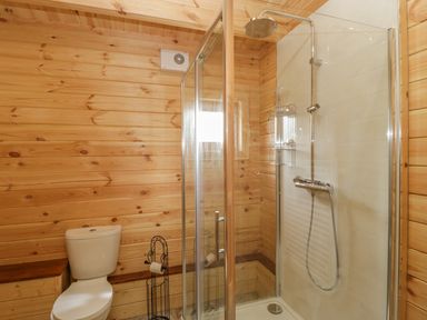 A bathroom with wooden walls a toilet and a glass enclosed shower at Sunnyside Lodge in Crewkerne