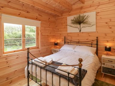 A bedroom with wooden walls and ceiling with a double bed and bedside tables at Sunnyside Lodge in Crewkerne