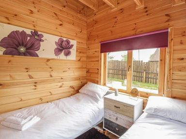 A bedroom with two beds a small chest of drawers a window with a purple blind and a floral painting on the wall at Sunnyside Lodge in Crewkerne