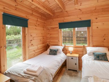 A bedroom with two single beds and a wooden nightstand with a lamp between the beds at Sunnyside Lodge in Crewkerne