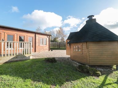 An outdoor area with a wooden building on the left and a small wooden hut on the right at Sunnyside Lodge in Crewkerne
